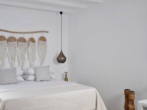 A bedroom with a bed, white bedding, a macrame wall hanging, a hanging light fixture, and wooden decor. - Maestro East Villa - Villa 2 (Πλάκα)
