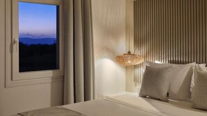 Une chambre avec une grande fenêtre, un lit agrémenté d’oreillers à motifs, une lampe suspendue et un mur à texture.