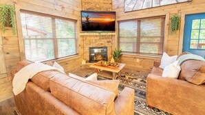 L’intérieur chaleureux d’un chalet avec une cheminée, des canapés en cuir et un téléviseur fixé au mur.