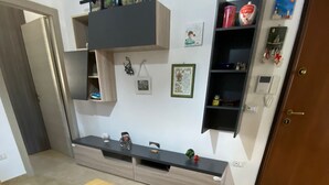 A room with a wooden table, a grey sofa, and a wall-mounted shelf with various items. - Vacation apartment (San Giorgio Ionico)