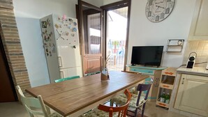 Une cuisine de taille réduite avec une table à manger en bois, deux chaises, un réfrigérateur, un téléviseur et une horloge au mur.