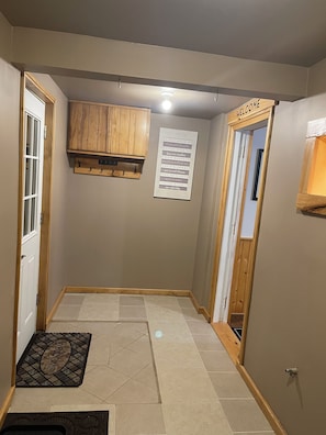 Un pasillo con una puerta de madera, felpudo, un tablón de anuncios y un armario.