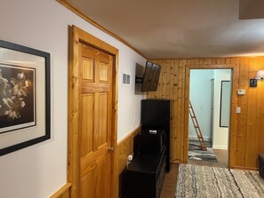 Un pasillo con paredes de madera, un cuadro enmarco, una puerta cerrada, un televisor montado en la pared y un armario negro.