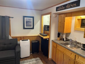 Un espacio habitable compacto con kitchenette, un sofá, un cuadro en la pared y un cartel sobre la puerta.