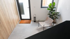 Ein modernes Interieur mit einem Korbstuhl, einem Topfpflanzen und einer Tür zu einem hellen Raum.