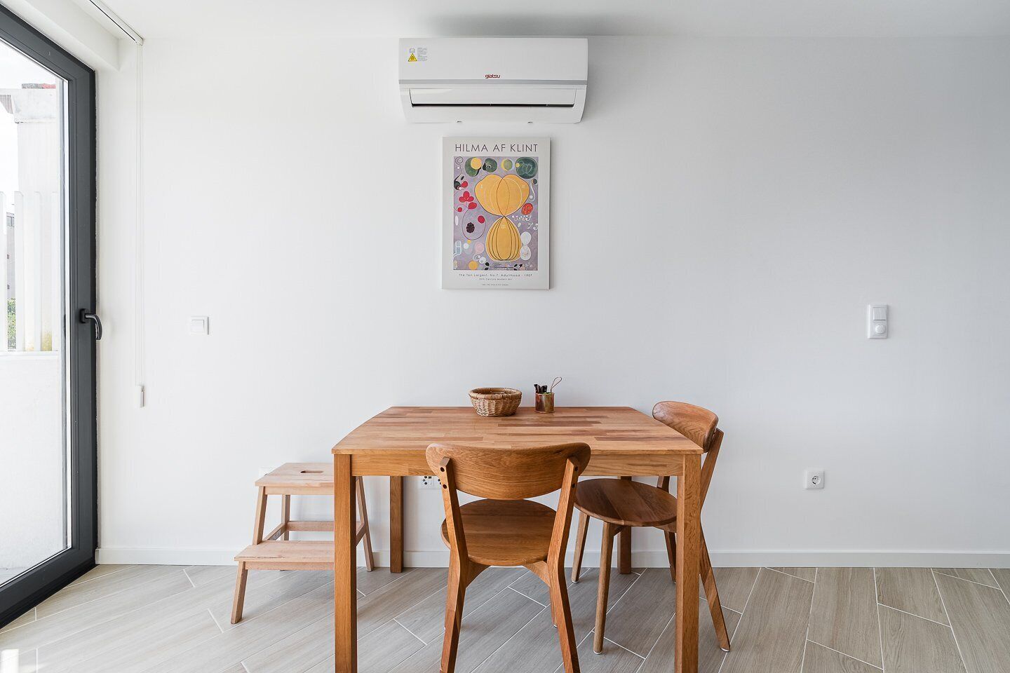 A dining area with a wooden table and chairs, a small side table, and a poster on the wall.