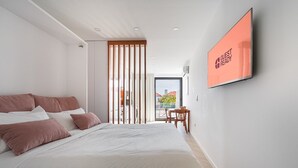 Ein modernes Schlafzimmer mit einem großen Bett, einem an der Wand montierten Fernseher und Blick ins Freie durch eine Schiebetür.
