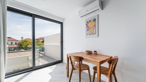 Ein Balkon mit Holztisch und -stühlen, einer Klimaanlage und einem gerahmten Kunstwerk.