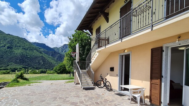 Une terrasse dallée de pierres, avec un escalier menant à un balcon, un vélo et une table entourée de chaises.