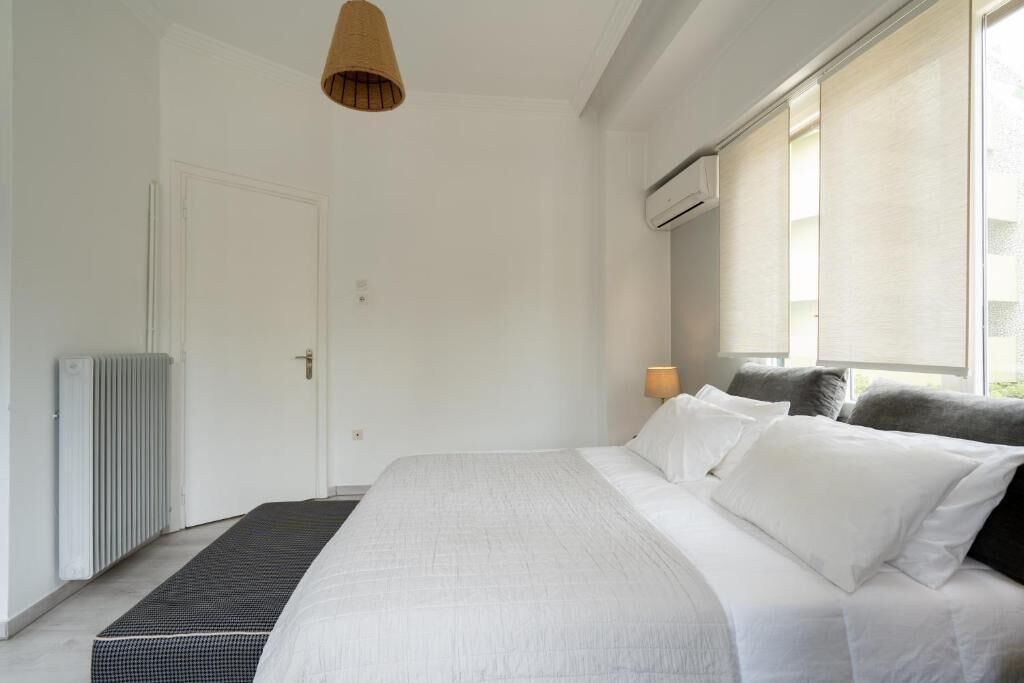 A modern hotel room with a large bed, a radiator, a window with blinds, and a hanging light fixture.