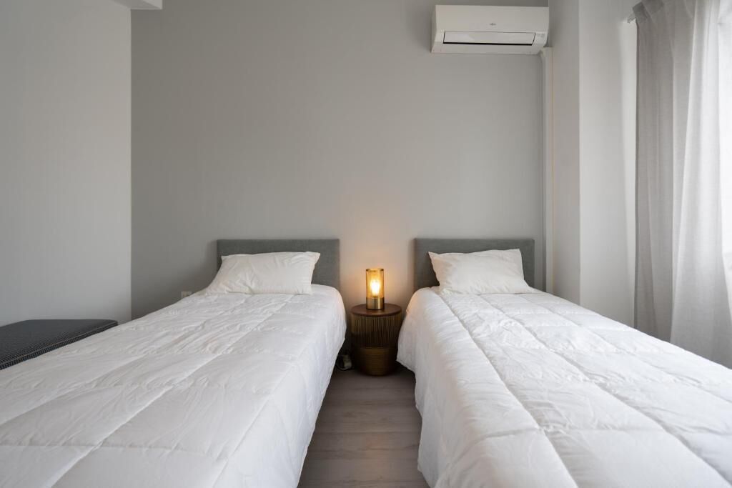 A hotel room with two single beds, a bedside table with a lamp, and an air conditioning unit on the wall.