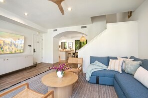 Ein modernes Wohnzimmer mit einem blauen Sofa, einem Holztisch und Korbstühlen.