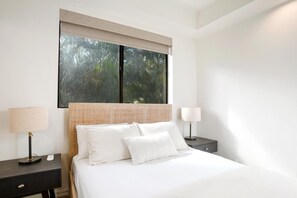 Ein Schlafzimmer mit einem großen Bett, zwei Nachttischen und einem Fenster mit Blick auf Bäume.