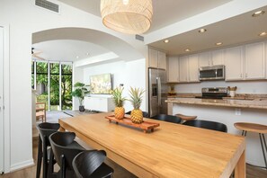 Une cuisine moderne avec des meubles blancs, des appareils en acier inoxydable et une table à manger en bois, accompagnée de chaises.