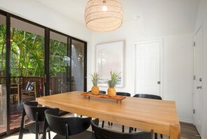 Un espace repas avec une table en bois, des chaises noires et un luminaire en matière tressée.