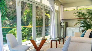 Una sala moderna con una mesa de vidrio, dos sillas, un sofá y un área de cocina con refrigerador y estufa.