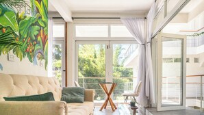 Una sala moderna con un sofá color beige, una mesa de centro de vidrio y un ventanal con cortinas.
