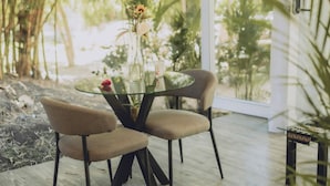Un área de comedor al aire libre moderna con una mesa de vidrio y dos sillas, rodeada de abundante follaje y vistas a un paisaje tropical.