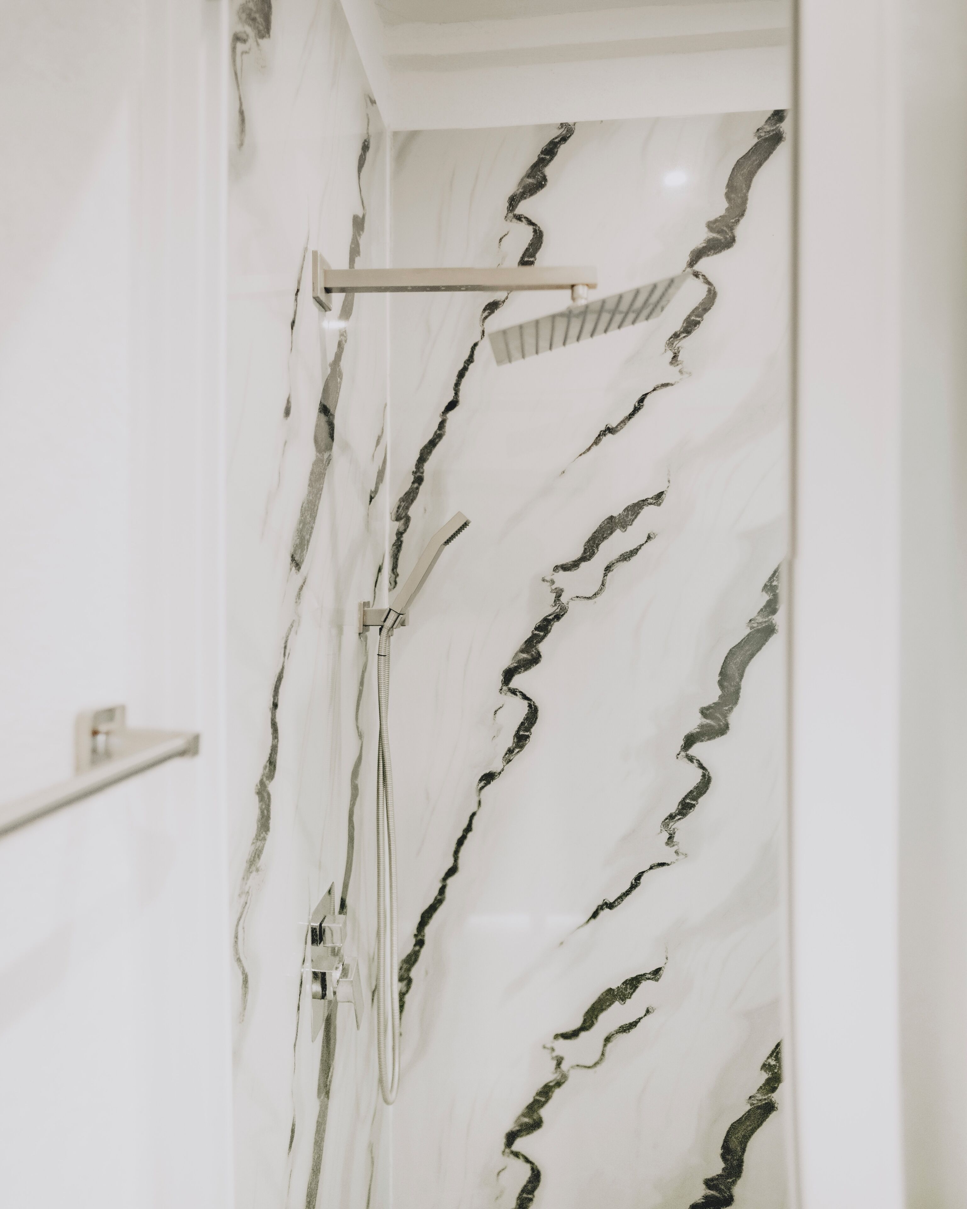 Un baño con ducha y pared de mármol.
