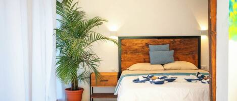 A bedroom with a wooden bed, a nightstand, a potted palm tree, and a window with curtains.