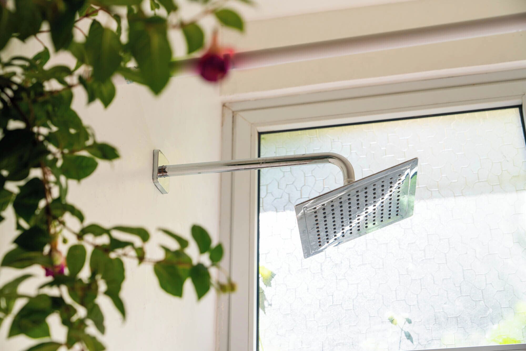 A showerhead mounted on a wall near a window with a geometric tile backsplash.