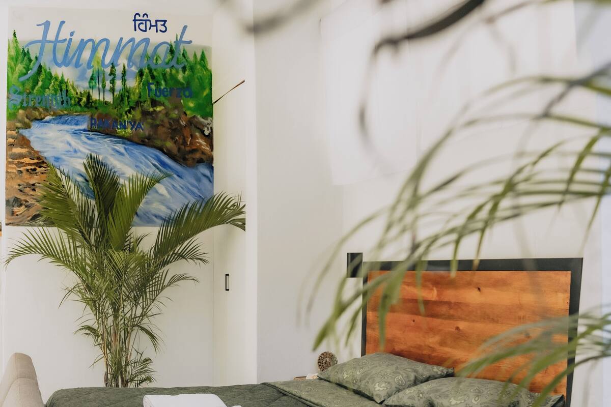 Un dormitorio con una cama, una mesita de noche, un cuadro colgado en la pared y una planta en maceta.