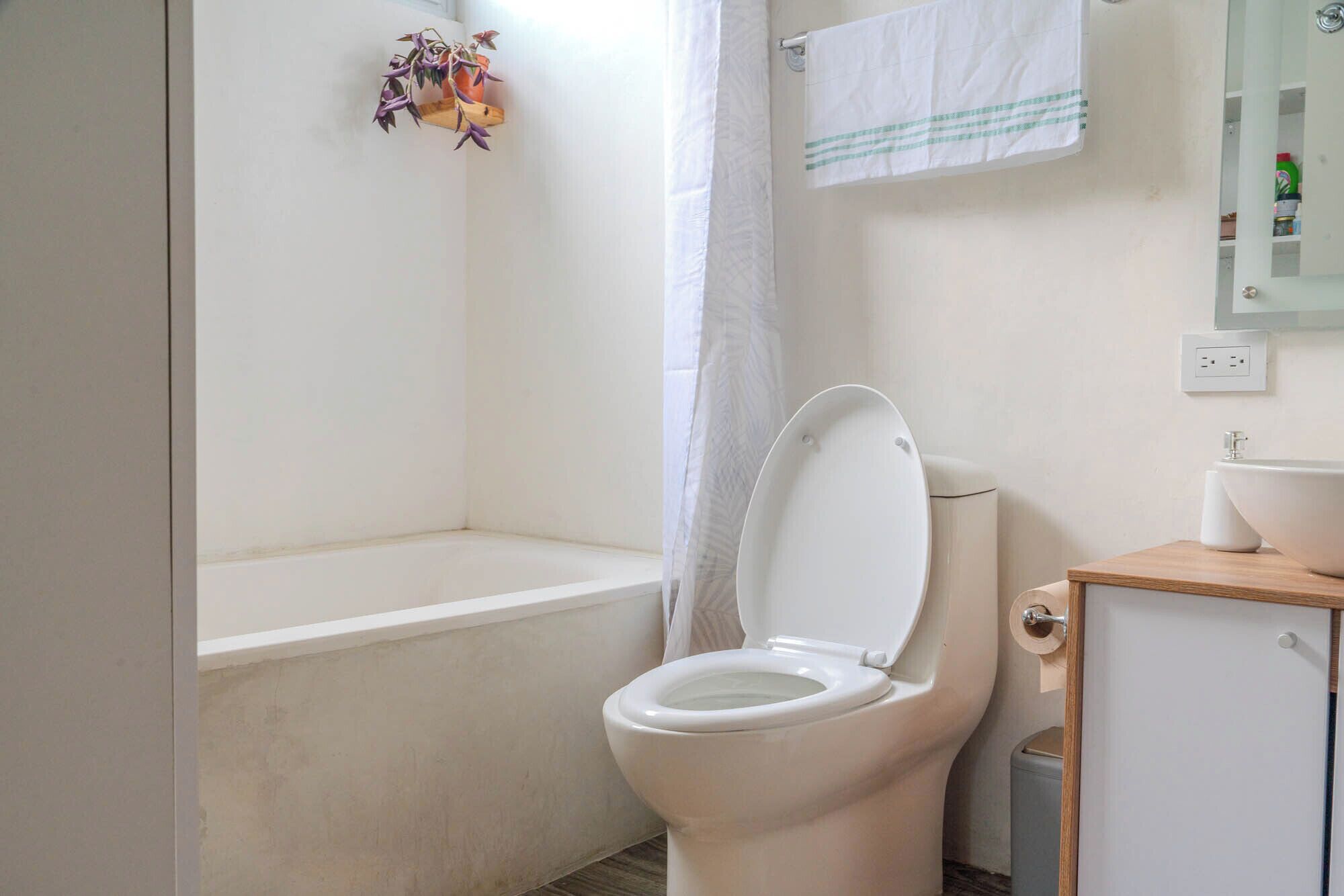 A bathroom with a toilet, a bathtub, a shower curtain, a towel rack, and a small wooden cabinet.