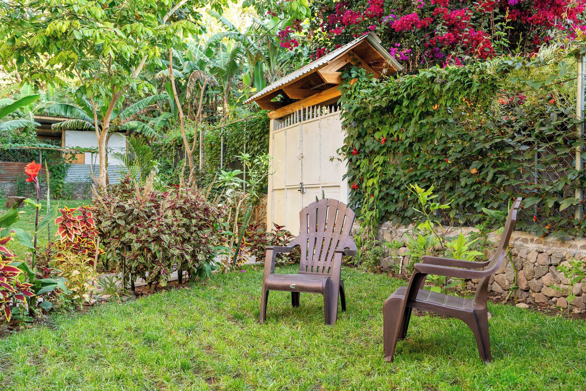 A garden with two wooden chairs, a small wooden structure, and various plants.