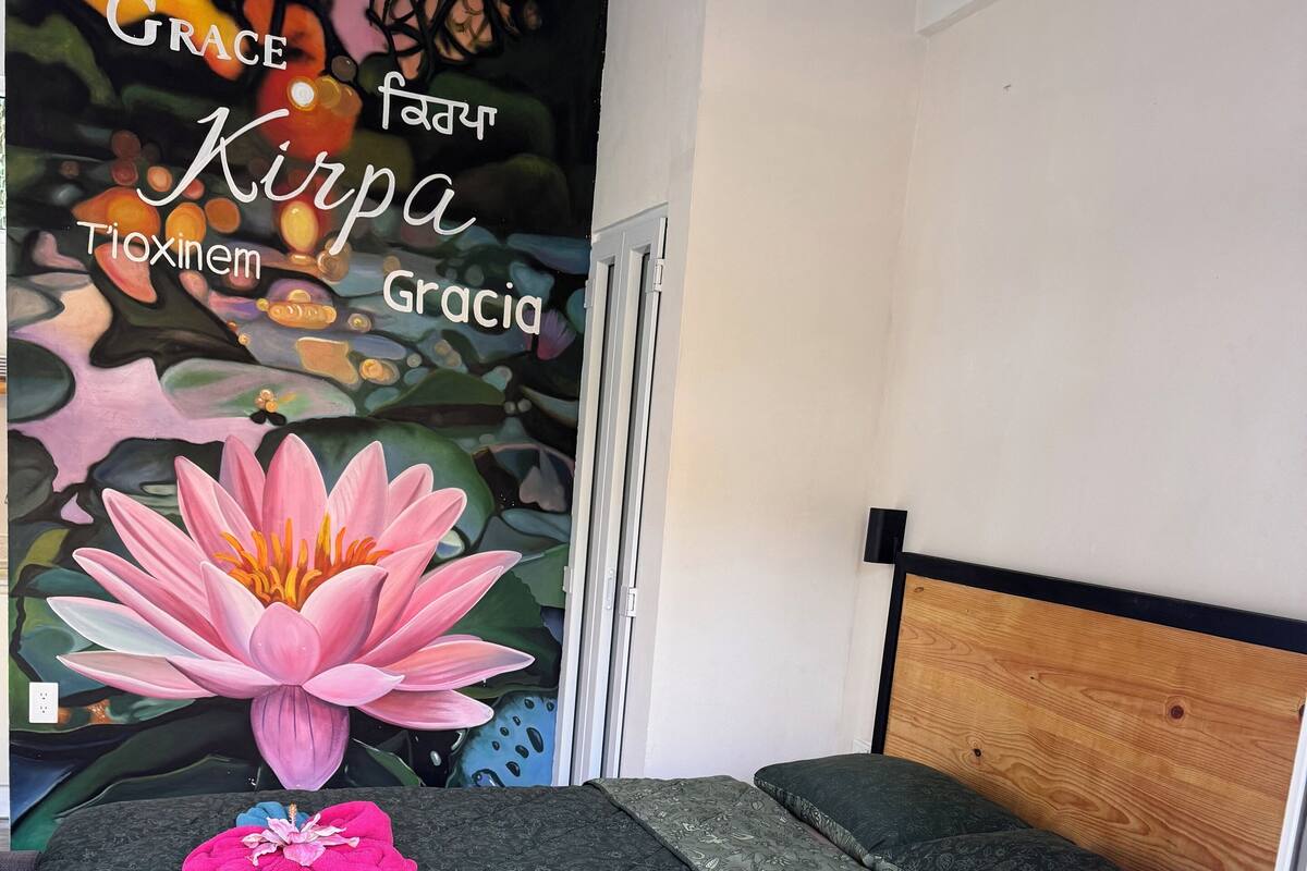 Un dormitorio con cama, cabecero de madera y un mural que incluye texto y una flor de loto.