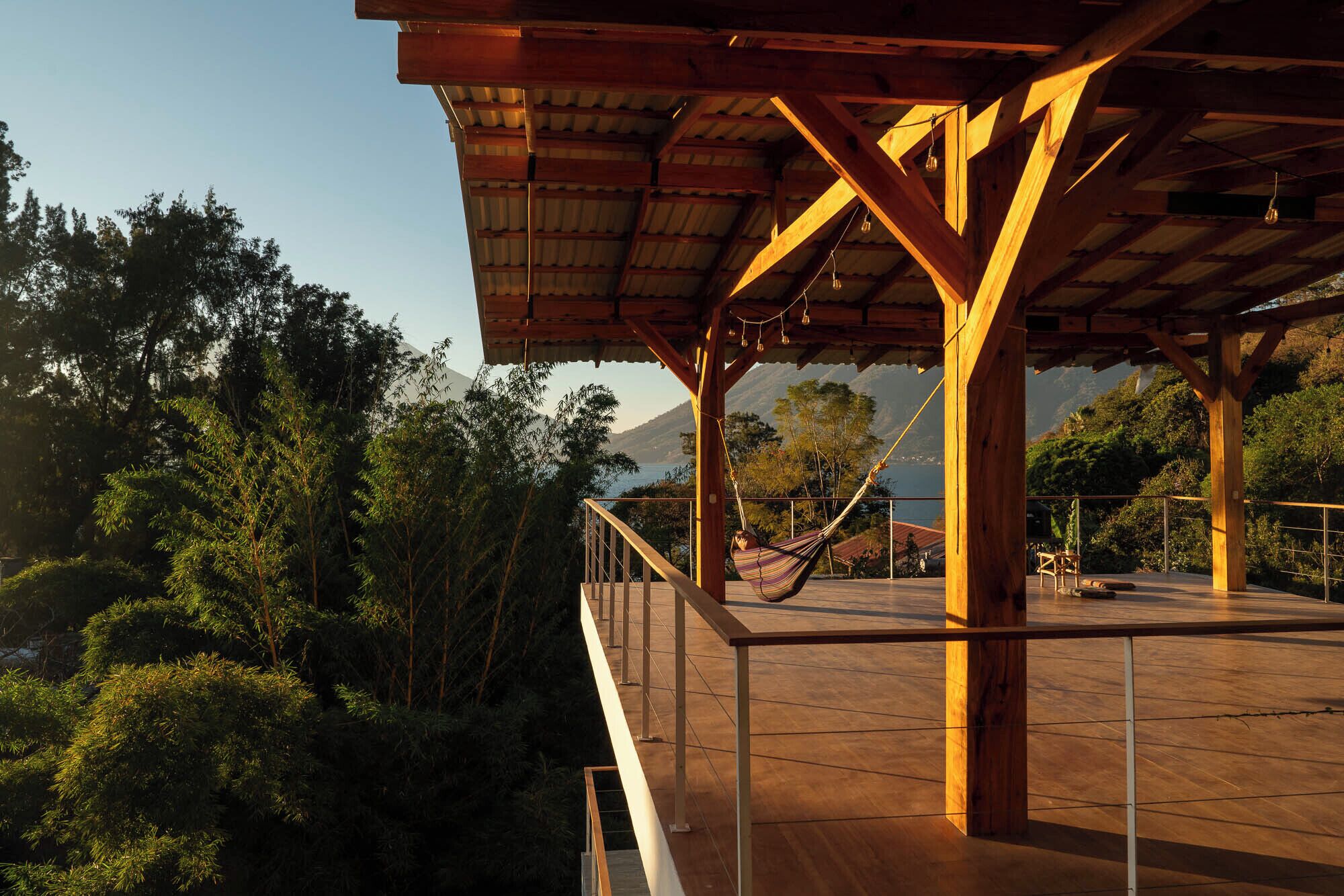 Una terraza de madera con una hamaca, rodeada de exuberante vegetación y montañas al fondo.