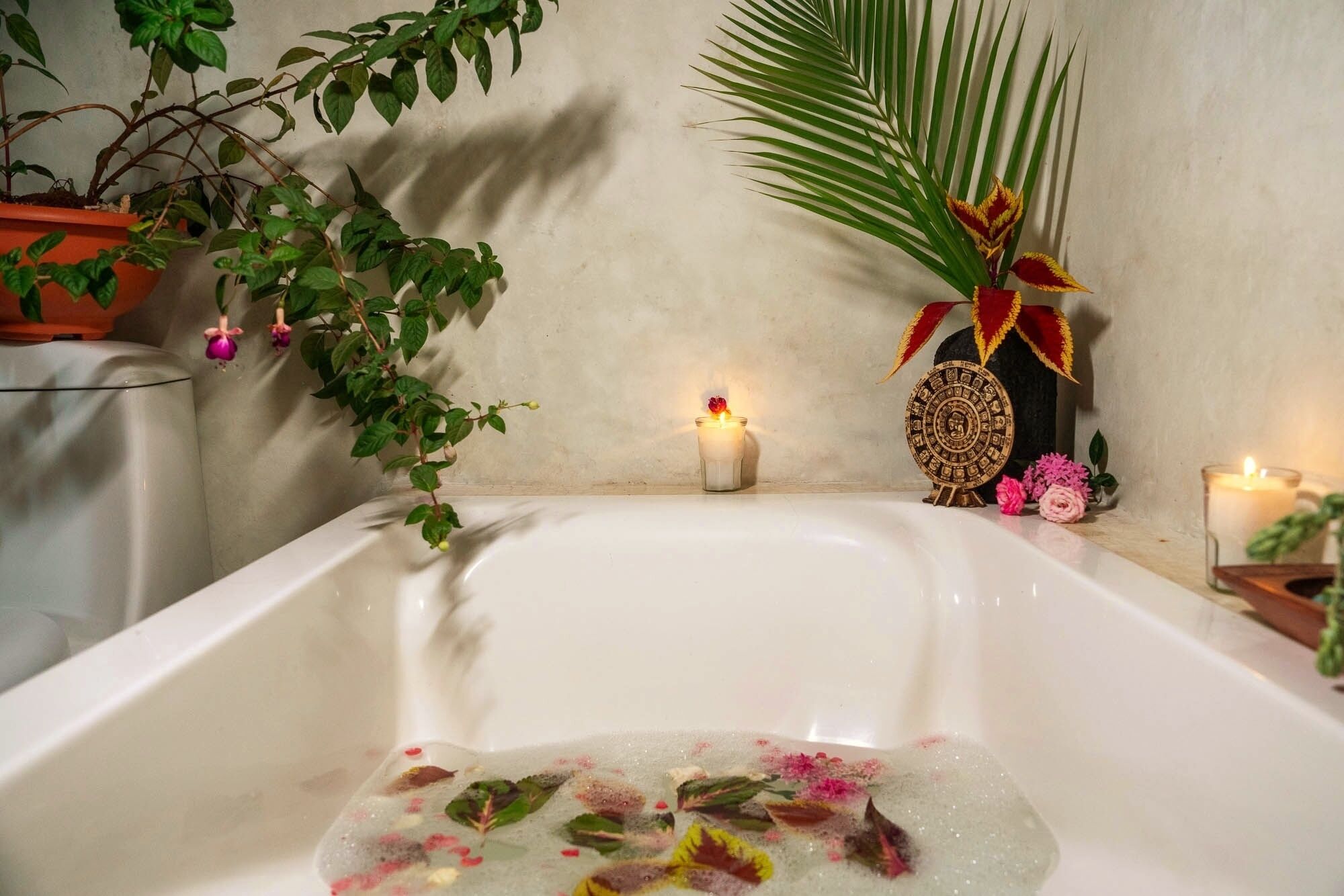 Une baignoire remplie d’eau, entourée de plantes et de bougies, suggérant un espace dédié à la détente et aux bains relaxants.