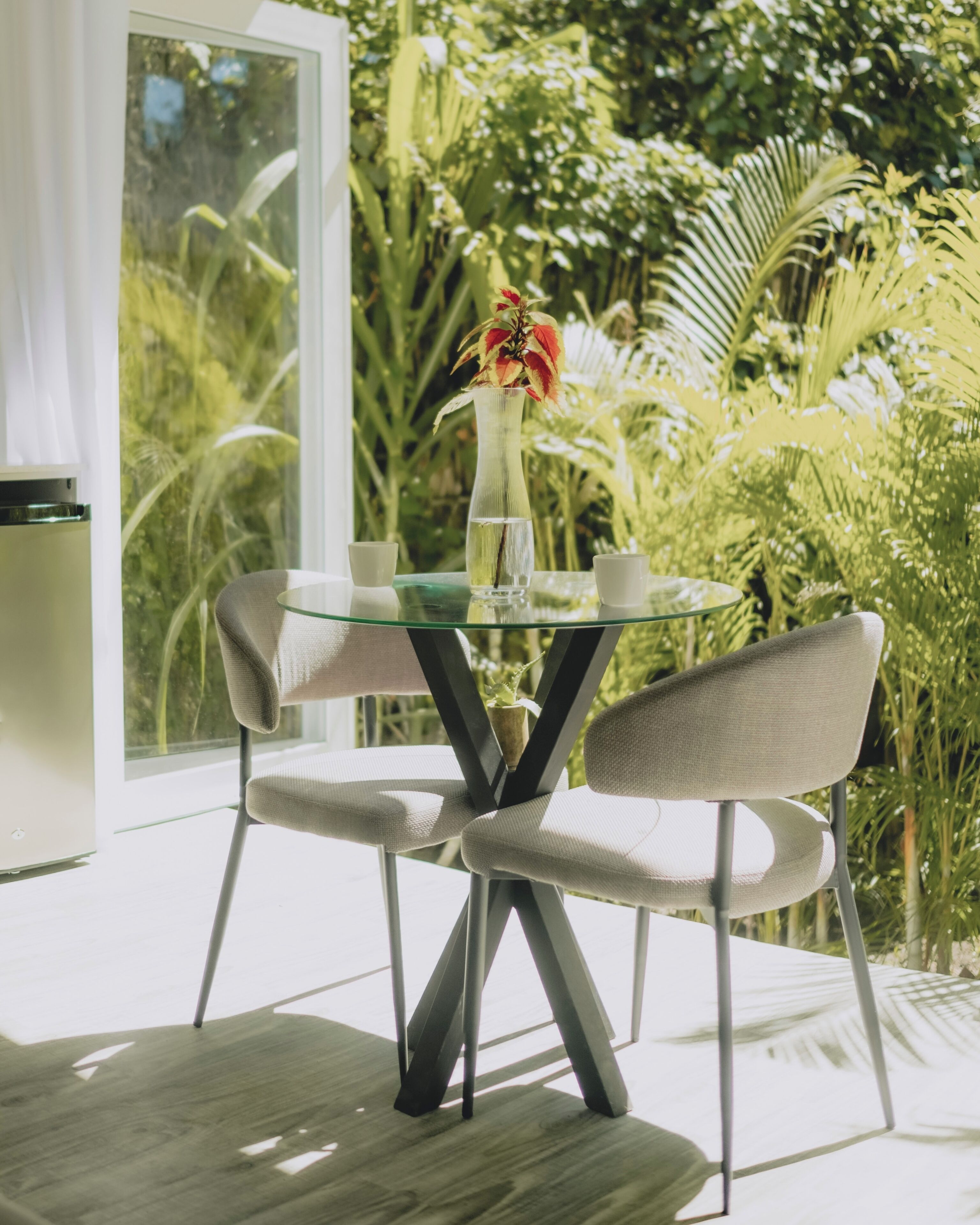 A glass table with two chairs, a vase with flowers, and a glass of water.