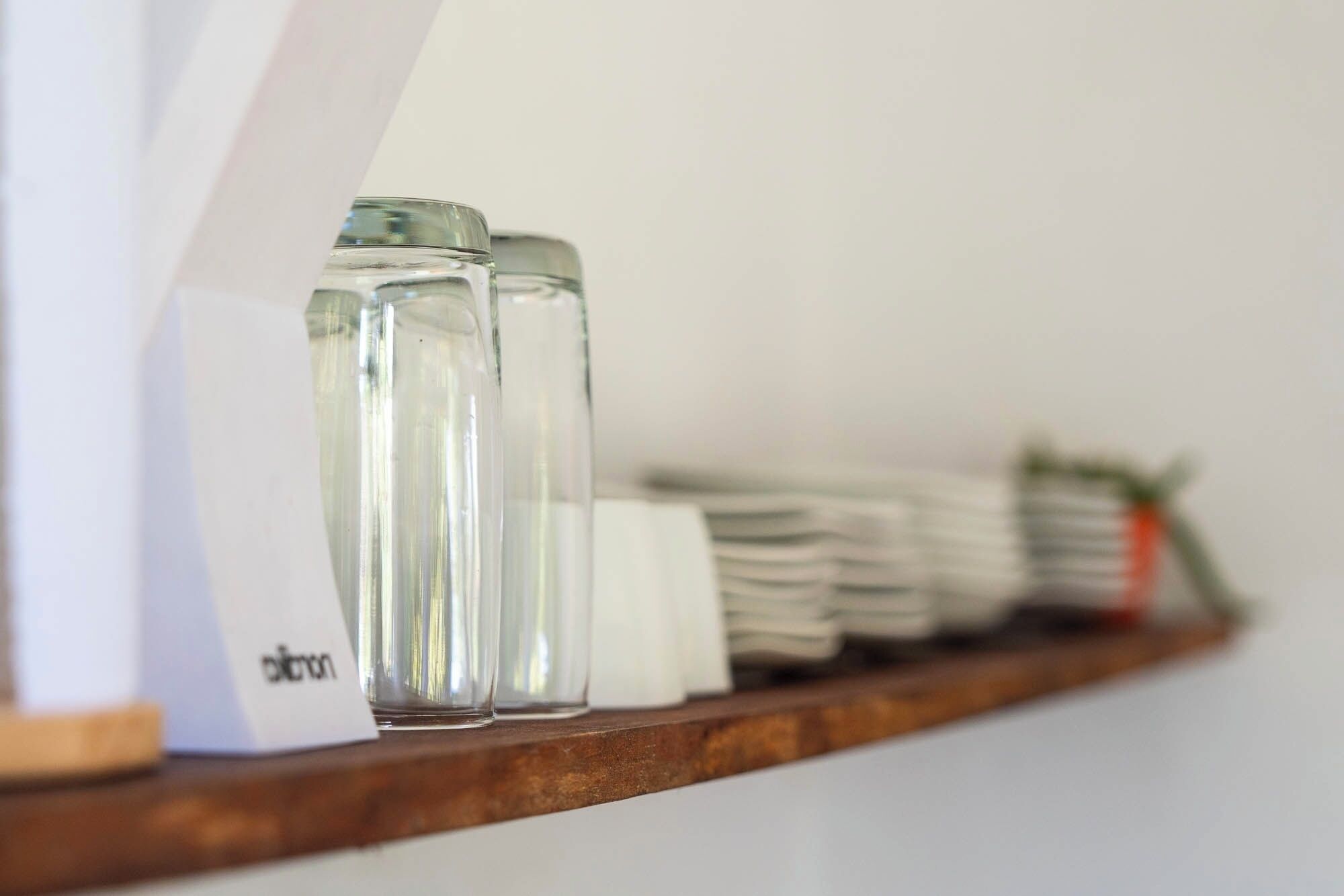 A wooden shelf with clear glass salt and pepper shakers, a stack of white napkins, and a small plant.