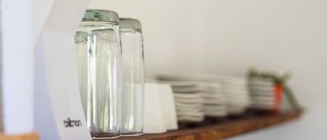 A wooden shelf with clear glass salt and pepper shakers, a stack of white napkins, and a small plant.