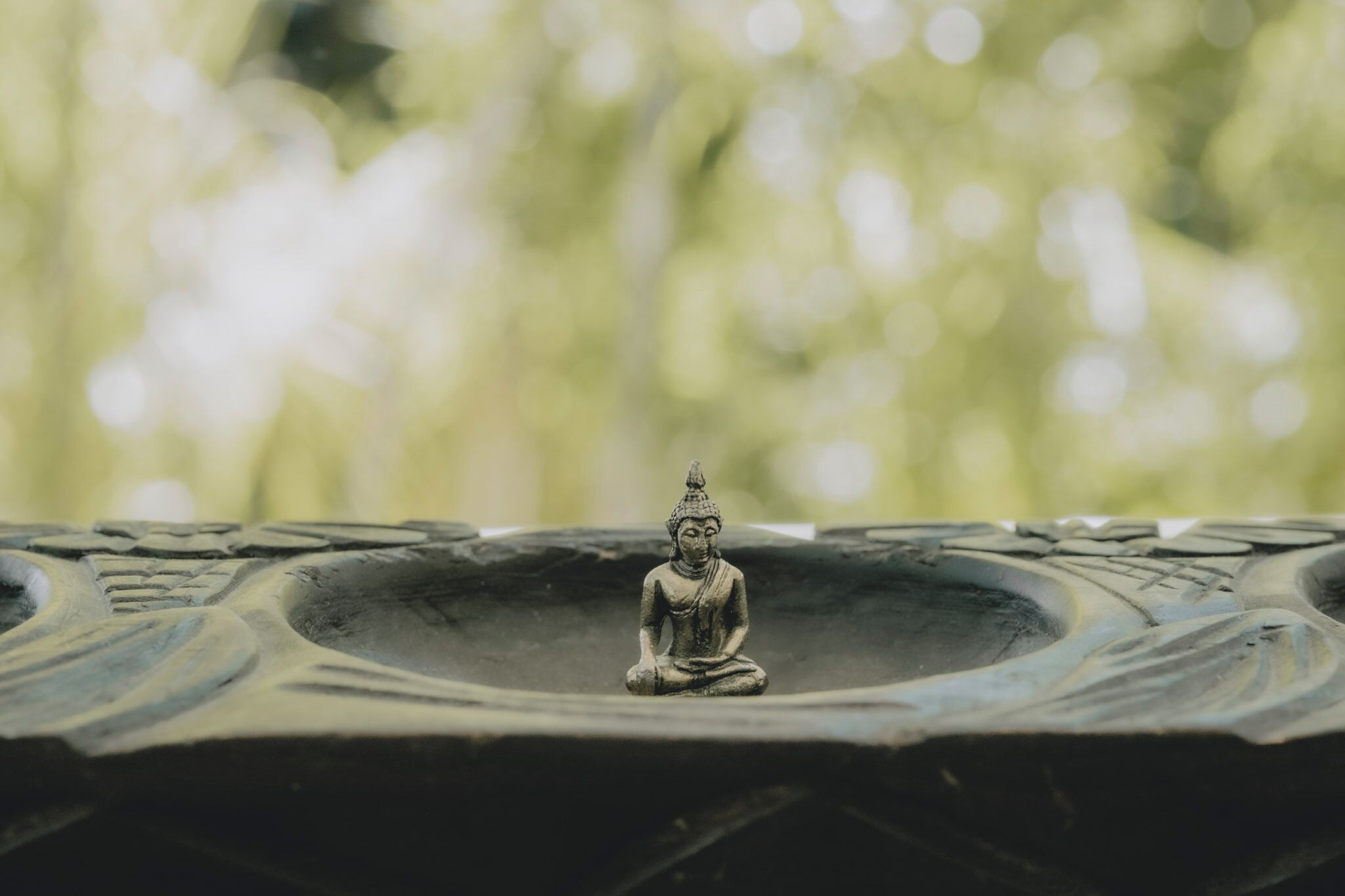 A Buddha statue on a stone pedestal with a blurred natural background.