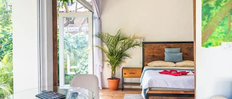 Un dormitorio con cama, mesita de noche, silla y vistas a zonas verdes por una ventana.