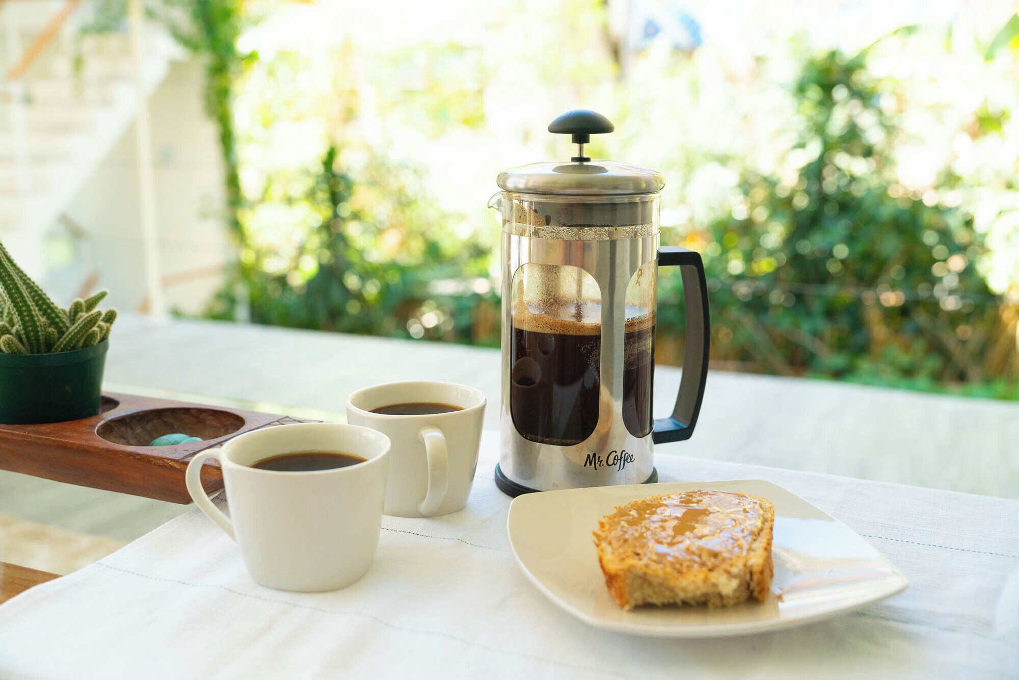 Une machine à café, deux tasses de café, une part de gâteau et un cactus sur une table.