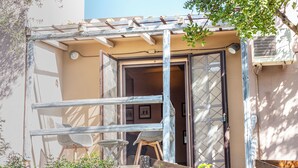 A building with a wooden pergola, a door with a glass panel, and a small table with chairs outside. - Accogliente Villa Immersa nel Verde con Incantevole Vista Mare (Sardegna)