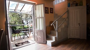 A room with a wooden staircase, a dining area with chairs and a table, and a door leading to an outdoor area. - Accogliente Villa Immersa nel Verde con Incantevole Vista Mare (Sardegna)