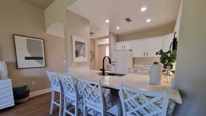 A modern kitchen with white cabinetry, a central island with bar stools, and recessed ceiling lighting. - Exceptional 3 bed and 3 bath Reunion Resort condo, with stunning golf views!  (Kissimmee)