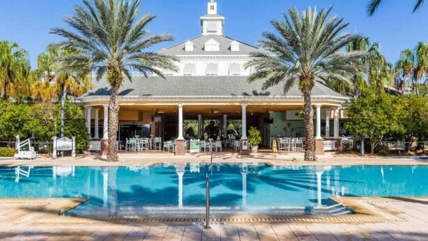 A pool area with a covered seating area, palm trees, and a building with a gabled roof. - Exceptional 3 bed and 3 bath Reunion Resort condo, with stunning golf views!  (Kissimmee)