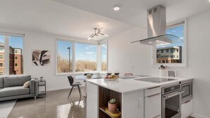 A modern kitchen with a central island, built-in oven, and a large window providing a view of the cityscape.