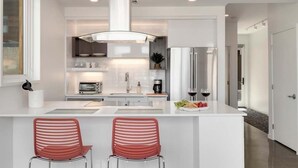 A modern kitchen with a central island, two red chairs, stainless steel appliances, and a large window.