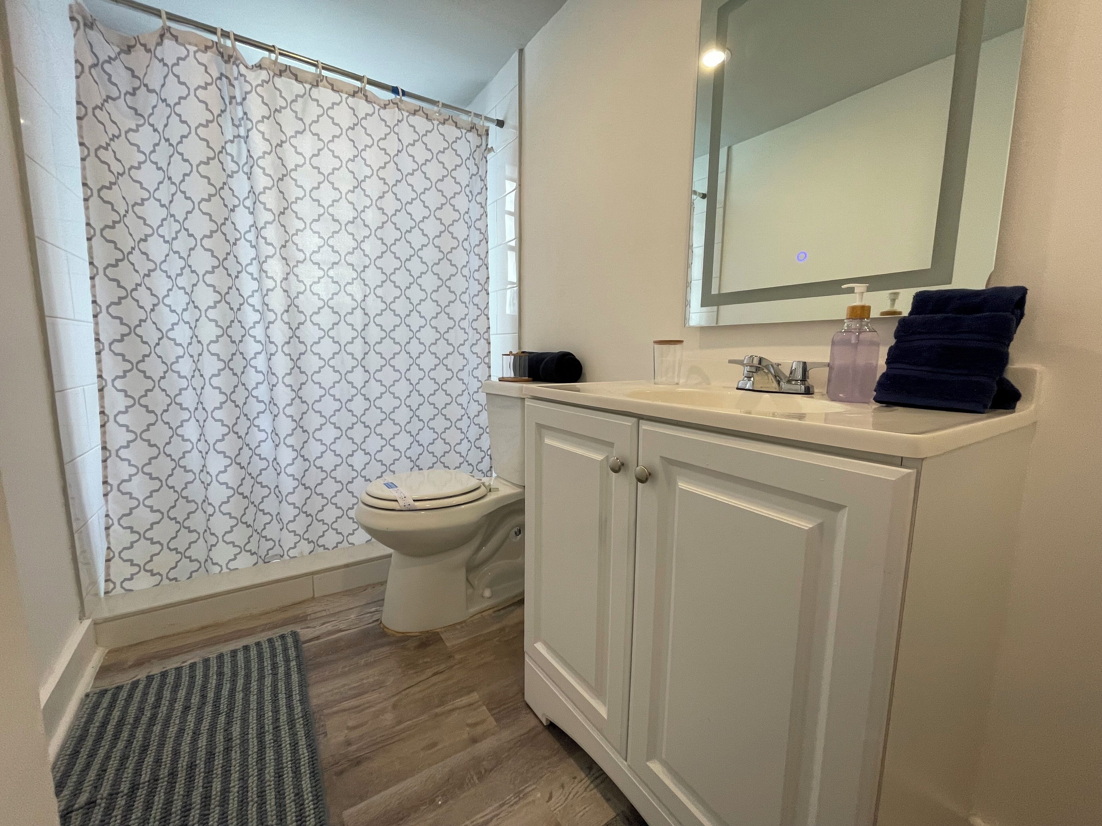 A bathroom with a shower curtain, toilet, sink, and cabinets.