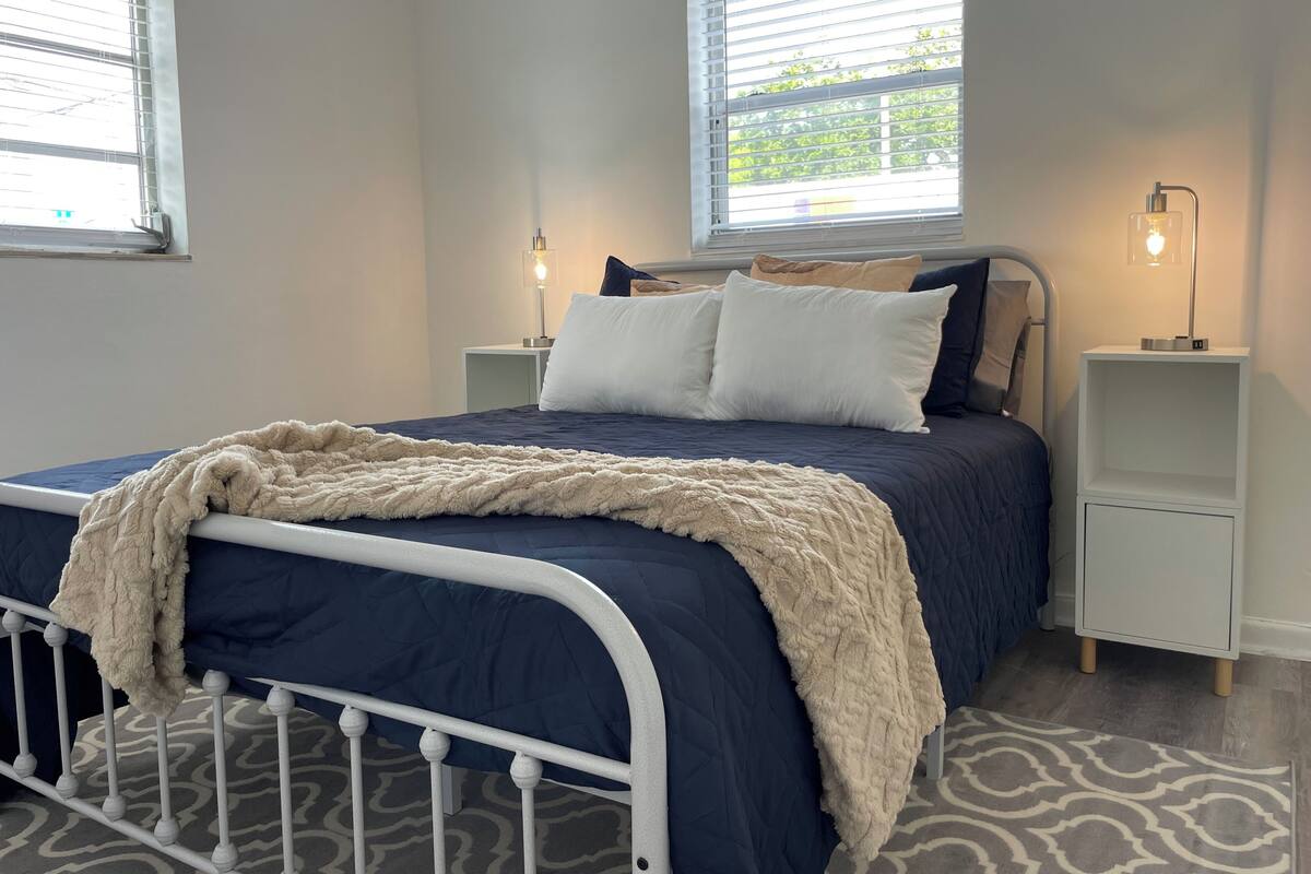 A bedroom with a bed, two bedside tables, a nightstand, a window, and a patterned rug.