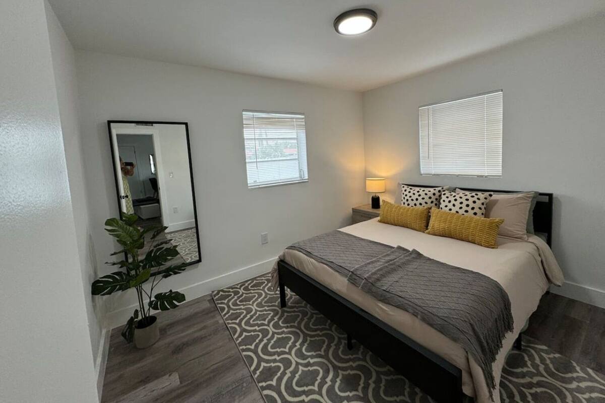 A bedroom with a bed, bedside lamps, a mirror, and a potted plant.