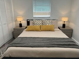 Une chambre bien rangée, avec un lit, deux tables de chevet et une fenêtre équipée de stores.
