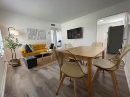 Un salon moderne avec une table à manger en bois, un canapé jaune et un téléviseur fixé au mur.