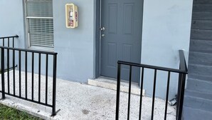 Edificio residenziale con una porta grigia, un estintore montato a parete e una finestra con persiane.