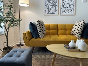 A mustard-colored sofa with polka dot pillows, a small round table with vases, a blue ottoman, and a floor lamp. - Remodeled apartments in little havana (Miami)